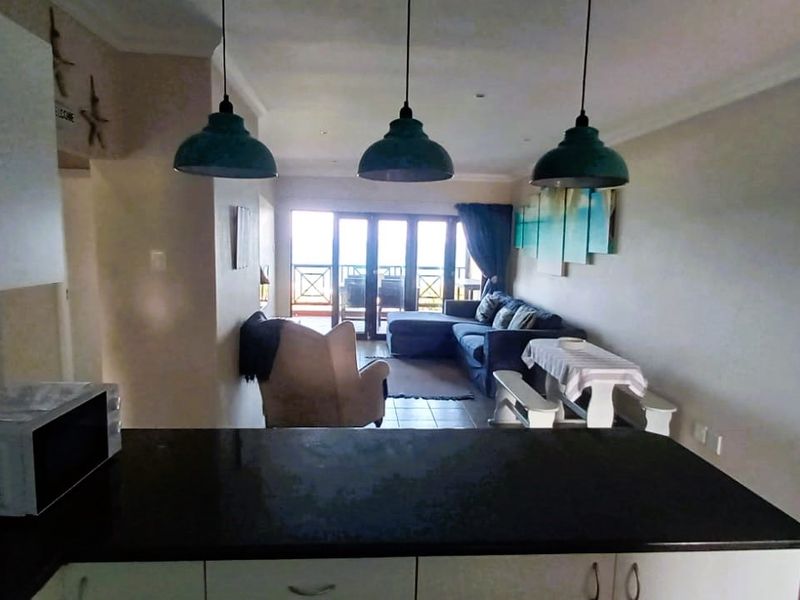Open plan living area featuring a kitchen with dark stone countertops, pendant lighting, and sliding glass doors leading to an outdoor balcony.
