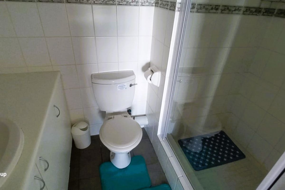A functional bathroom featuring a vanity with integrated sink, a standard toilet, and a glass-enclosed shower with tiled wall finishes.