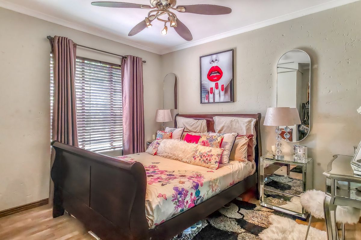 A well-lit bedroom featuring laminate flooring, a ceiling fan, and window blinds, providing a comfortable and functional living space.