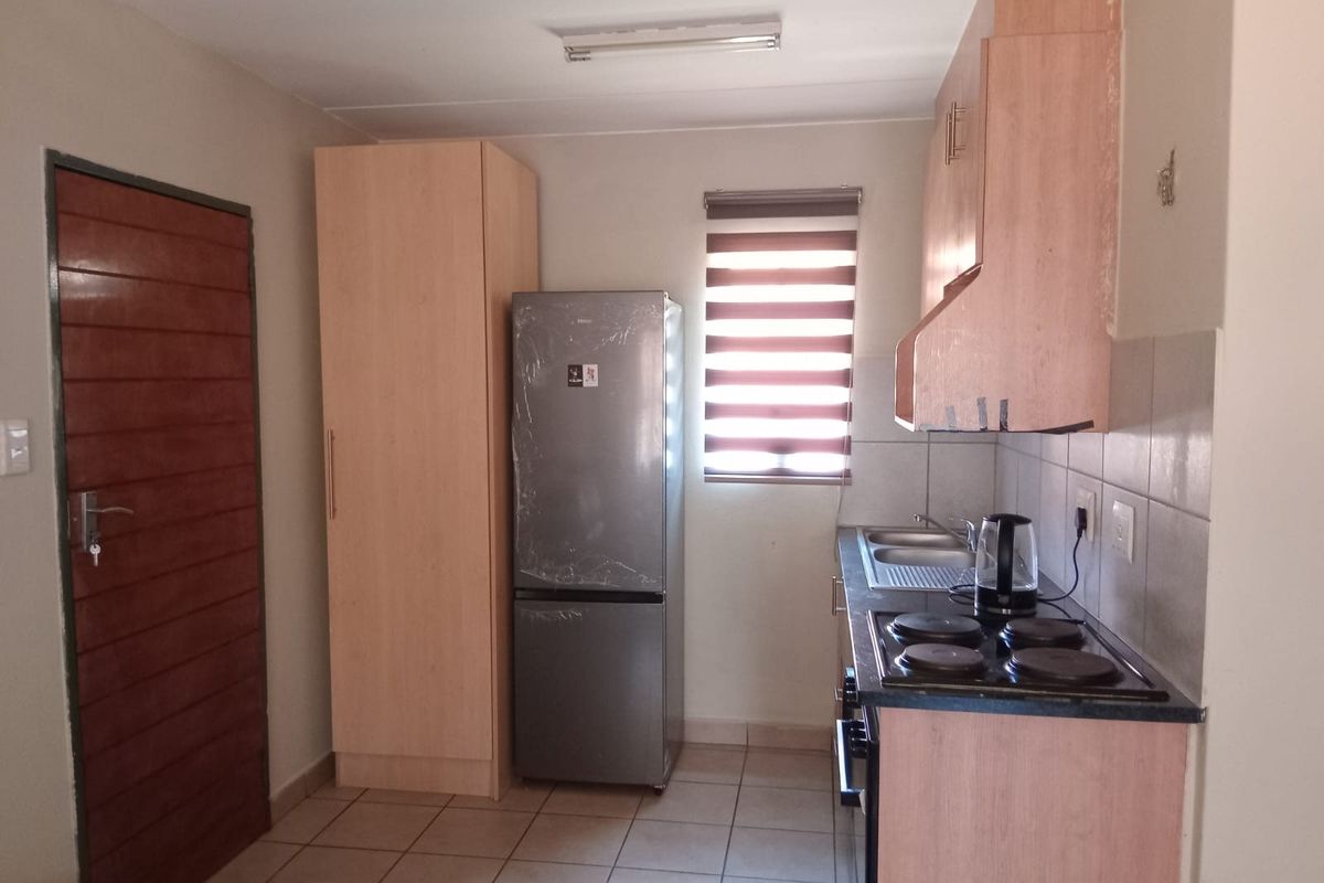 Compact kitchen featuring light wood-finish cabinetry, tiled flooring, a built-in electric hob, and a stainless steel sink.