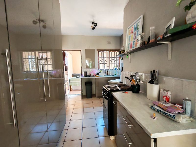 A functional kitchen featuring built-in cabinetry, tiled flooring, a stainless steel sink, and a tiled backsplash, with direct access to an adjacent utility area.