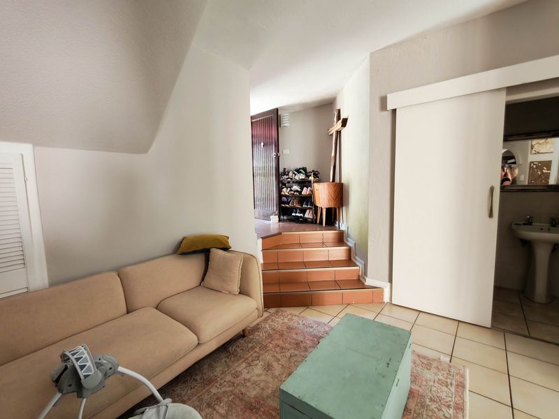 Living area featuring tiled flooring, a sliding door leading to an adjacent bathroom with a pedestal basin, and a small staircase.