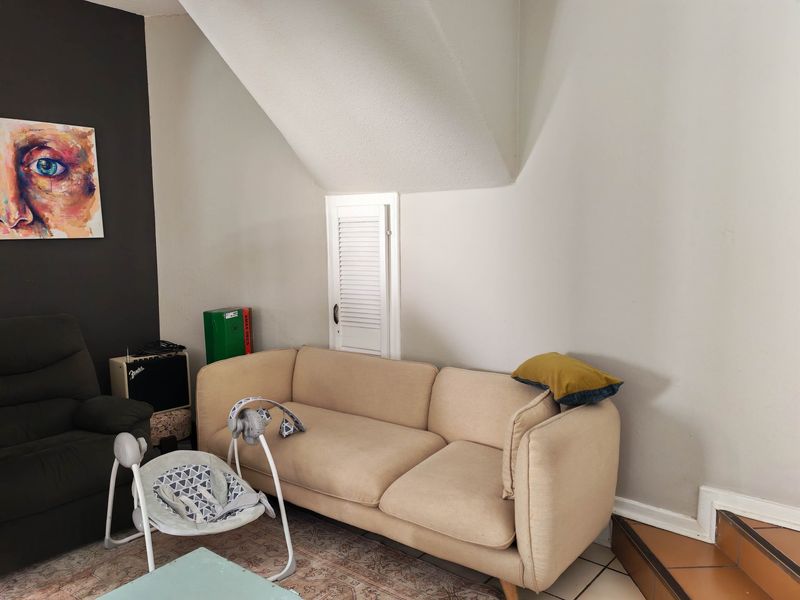 A living room area featuring a sloped ceiling, a small louvered access door, and tiled stairs leading to an upper level.
