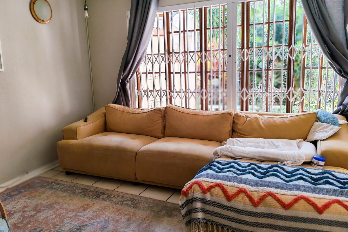 A living room featuring tiled flooring and a large sliding glass door with integrated security gate, providing natural light and garden access.