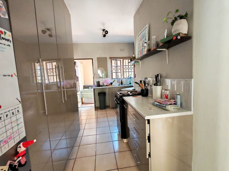 A functional galley-style kitchen featuring modern high-gloss cabinetry, tiled flooring, a freestanding stove, and a double sink with a tiled backsplash.