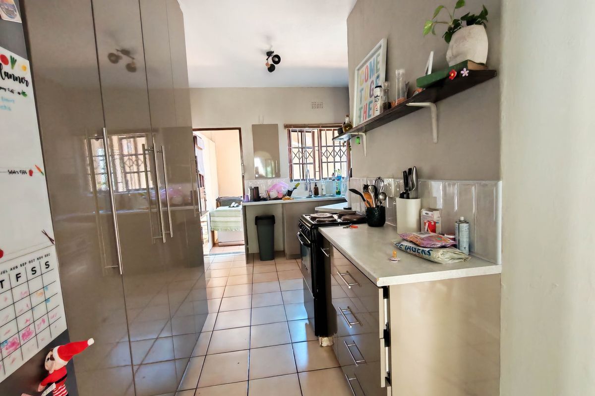 A functional galley-style kitchen featuring modern high-gloss cabinetry, tiled flooring, a freestanding stove, and a double sink with a tiled backsplash.