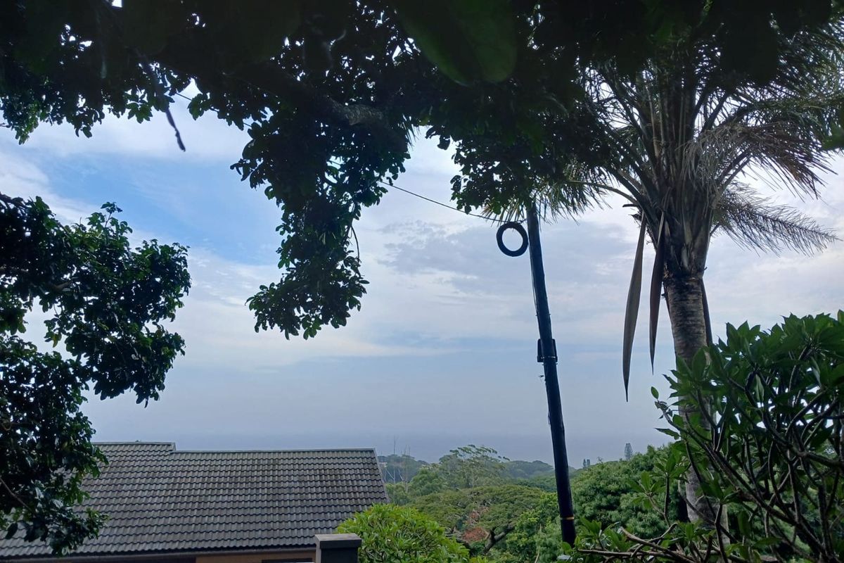 A scenic elevated view overlooking lush greenery and a residential tiled roof, framed by mature trees.