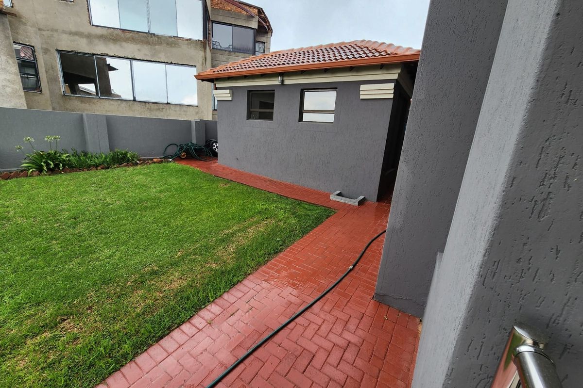 A rear garden area featuring a well-maintained lawn, red brick paved pathways, and a detached outbuilding with a tiled roof.