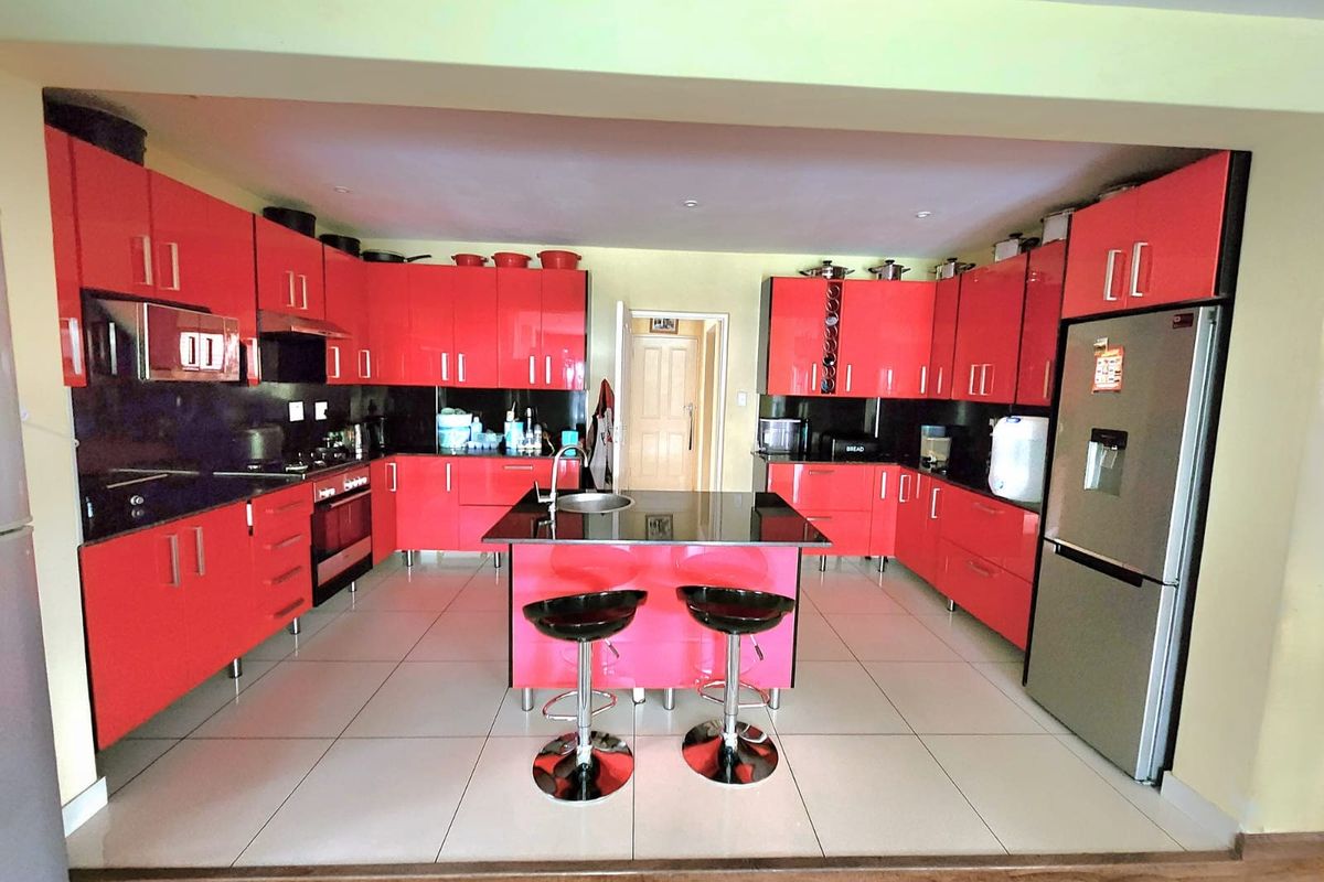 A spacious kitchen featuring vibrant red cabinetry, a central island with a sink, and tiled flooring, offering a bold and functional cooking space.