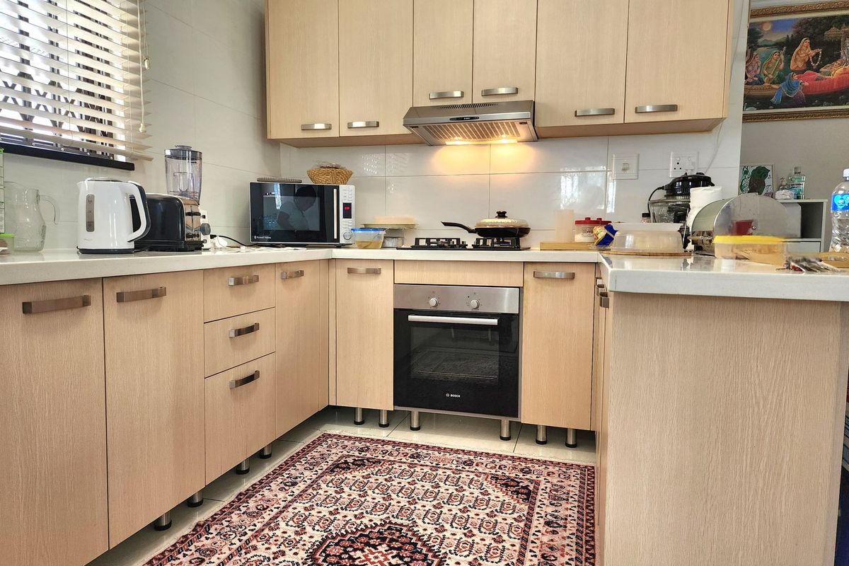 A functional kitchen featuring light wood cabinetry, stone countertops, a built-in oven, gas hob, and an extractor fan with a tiled backsplash.