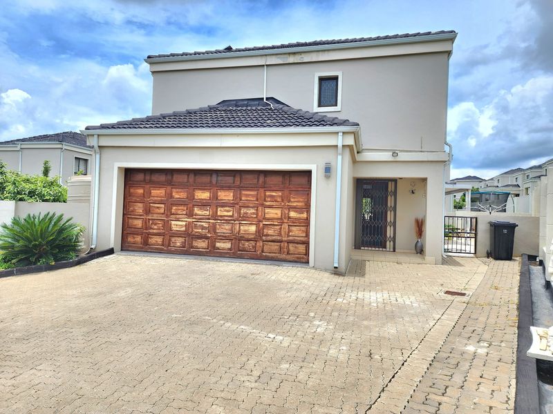 Front elevation of a double-storey cluster home featuring a paved driveway, a double garage with a weathered wooden door, and a secure entrance.