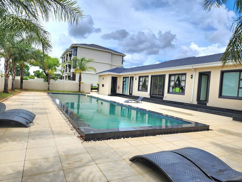 A well-maintained outdoor pool area featuring a rectangular swimming pool with tiled decking and direct access to the main residence.