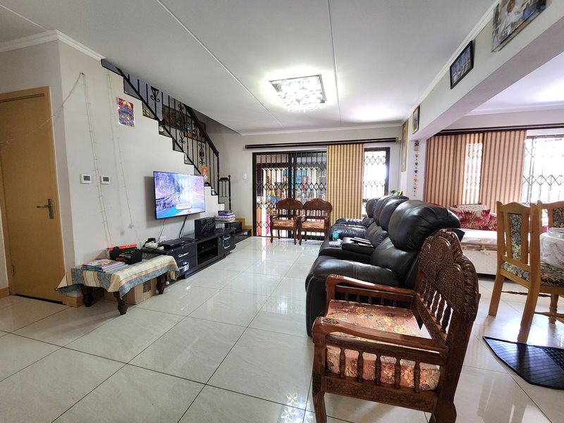 Spacious open-plan living area featuring tiled flooring, a staircase with wrought iron railing, and direct access to the exterior through a security gate.