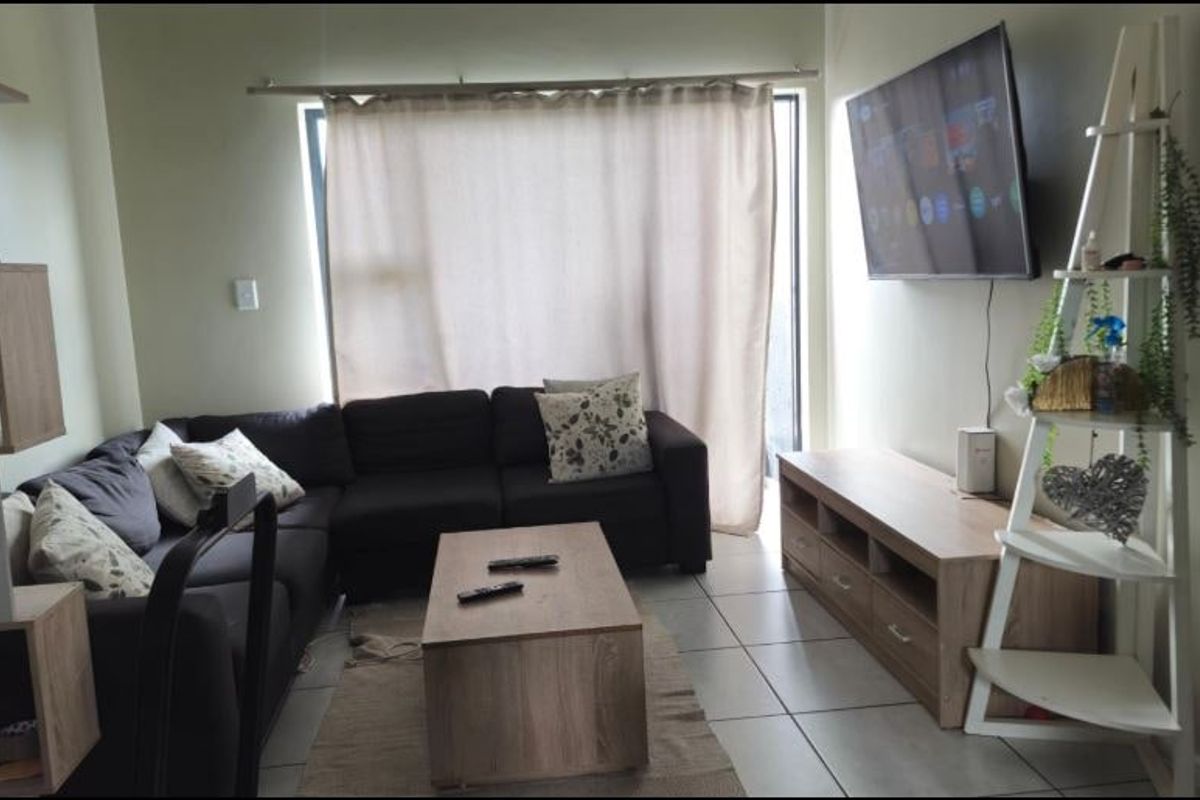 A comfortable living room featuring tiled flooring and a large window with curtain rails, providing a functional and well-lit space.