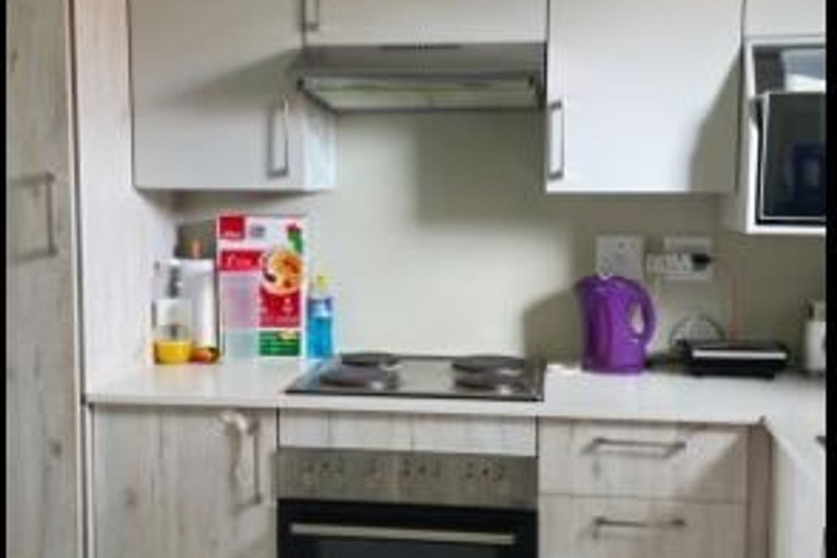 A functional kitchen featuring modern light-wood cabinetry, a built-in oven, electric hob, and an integrated extractor fan with tiled flooring.