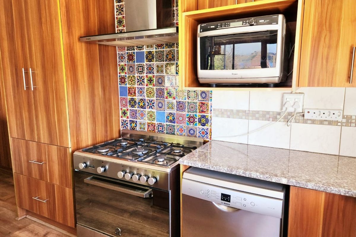 A functional kitchen featuring wood-grain cabinetry, granite countertops, a gas stove with an extractor fan, and a vibrant mosaic tile splashback.