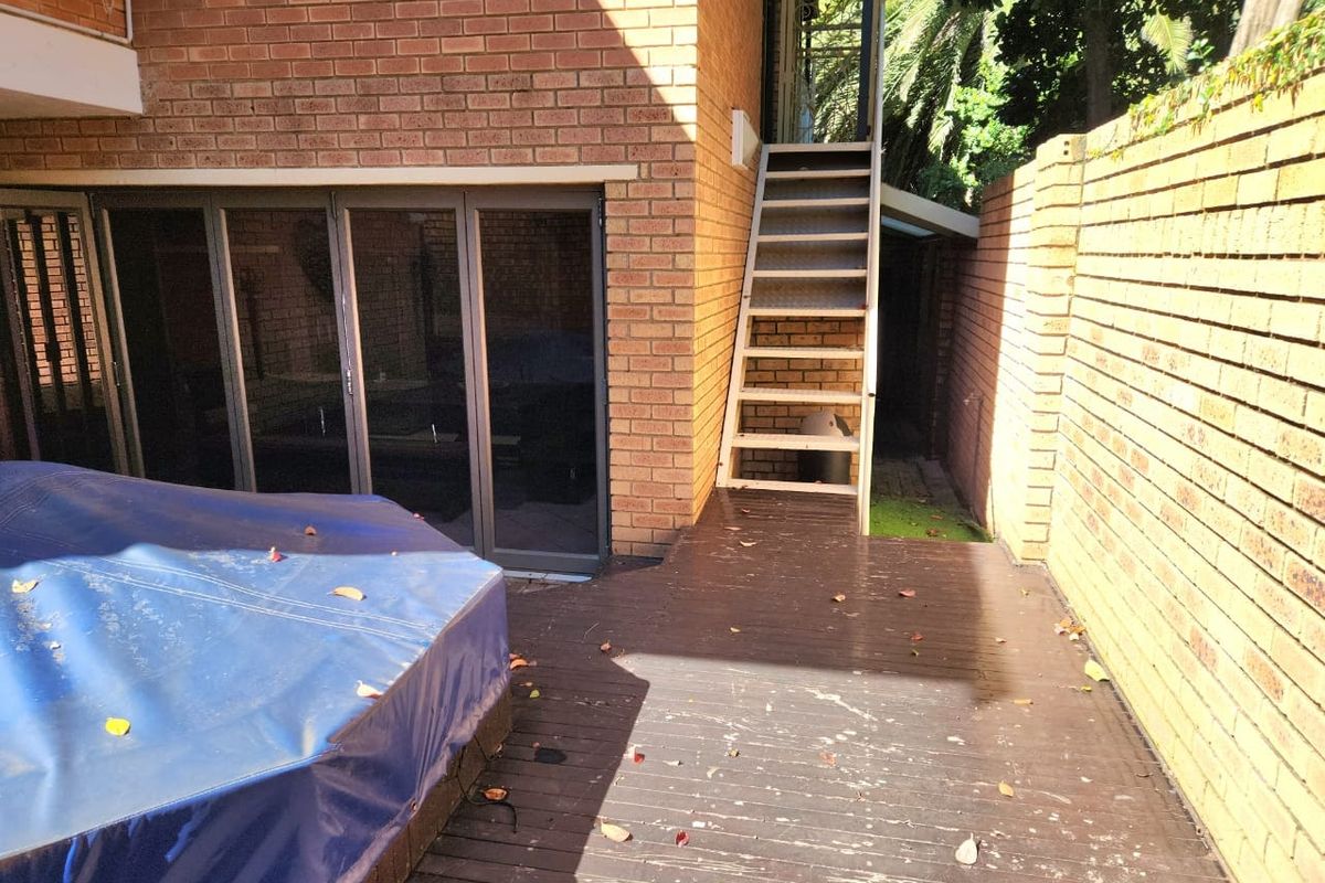 Rear exterior area featuring timber decking, brick walls, and an external staircase leading to an upper level, with sliding glass door access.