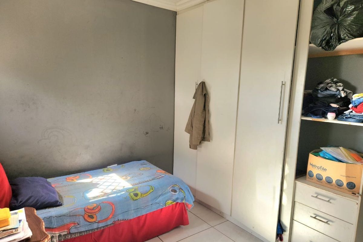 A bedroom featuring tiled flooring and a built-in wardrobe with white cabinetry. The room requires cosmetic updates to the wall finishes.