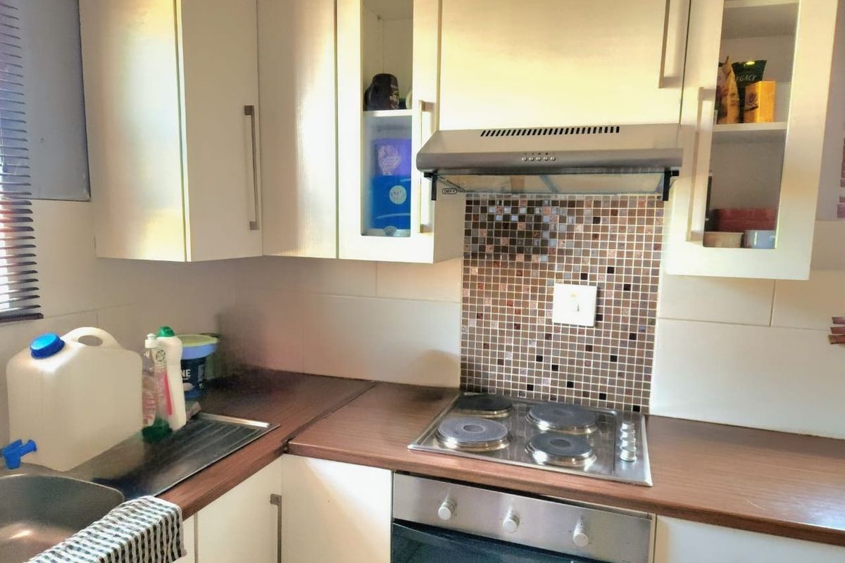A functional kitchen featuring white cabinetry, laminate countertops, a mosaic tile splashback, and integrated electric cooking appliances.