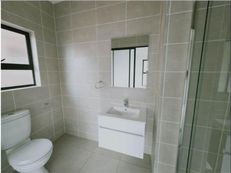 Modern bathroom featuring a wall-mounted vanity, glass shower enclosure, and neutral floor-to-ceiling tiling.