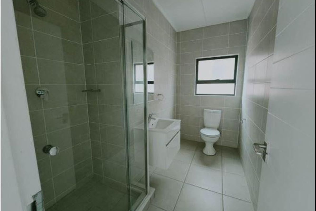 A modern, clean bathroom featuring a glass-enclosed shower, wall-mounted vanity, and neutral floor-to-ceiling tiling.