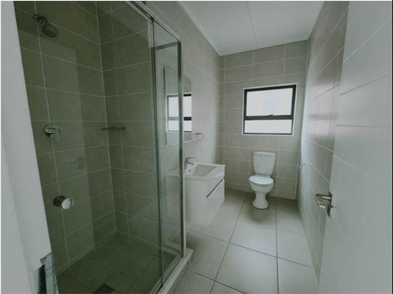 A modern, clean bathroom featuring a glass-enclosed shower, wall-mounted vanity, and neutral floor-to-ceiling tiling.
