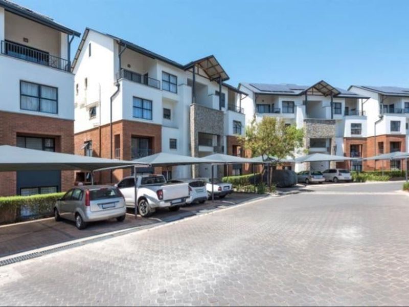 Exterior view of a modern apartment complex featuring brick and plaster facades, private balconies, and dedicated covered parking bays for residents.