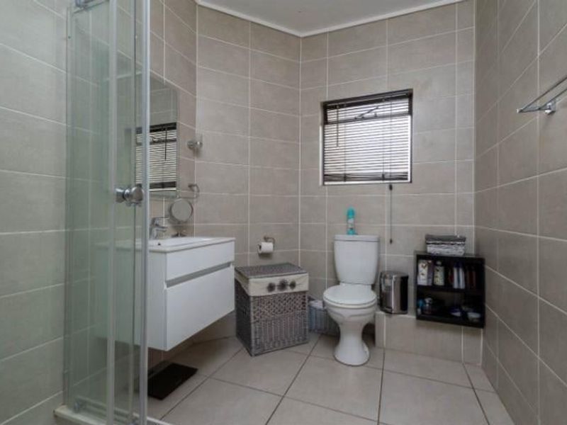 A clean and functional bathroom featuring a wall-mounted vanity, a glass shower enclosure, and neutral floor-to-ceiling wall tiling.