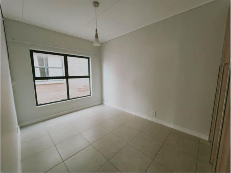A clean, empty bedroom featuring neutral tiled flooring, built-in cupboards, and a simple pendant light fixture, offering a blank canvas for personalization.