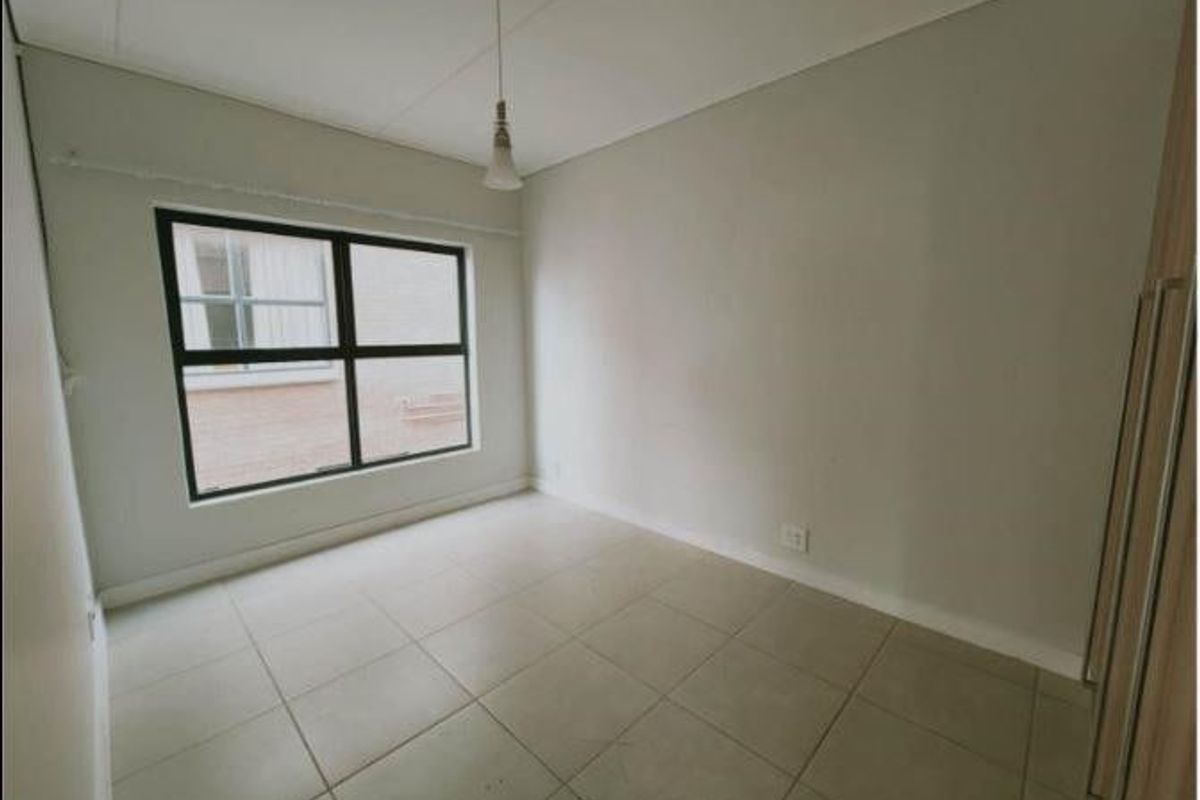 A clean, empty bedroom featuring neutral tiled flooring, built-in cupboards, and a simple pendant light fixture, offering a blank canvas for personalization.
