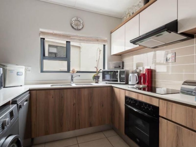 A well-maintained kitchen featuring modern wood-finish cabinetry, stone-look countertops, integrated appliances, and a tiled backsplash with a functional layout.