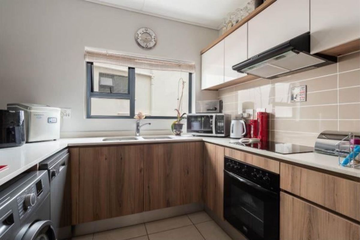 A well-maintained kitchen featuring modern wood-finish cabinetry, stone-look countertops, integrated appliances, and a tiled backsplash with a functional layout.