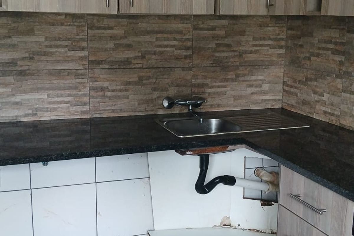 Kitchen area featuring granite countertops and wood-look cabinetry, currently requiring repairs to the lower cabinet base and plumbing enclosure.