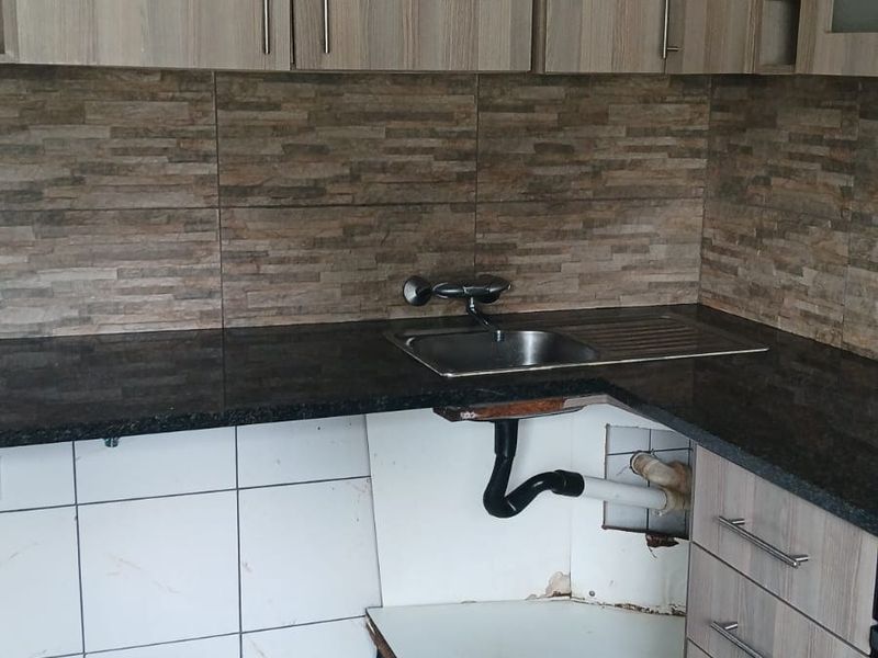 Kitchen area featuring granite countertops and wood-look cabinetry, currently requiring repairs to the lower cabinet base and plumbing enclosure.