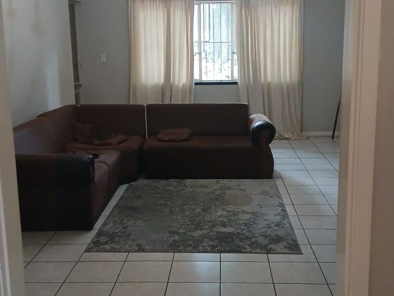 A living room featuring ceramic floor tiles, a central chandelier, and a window fitted with security bars.