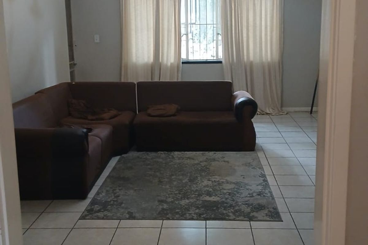 A living room featuring ceramic floor tiles, a central chandelier, and a window fitted with security bars.