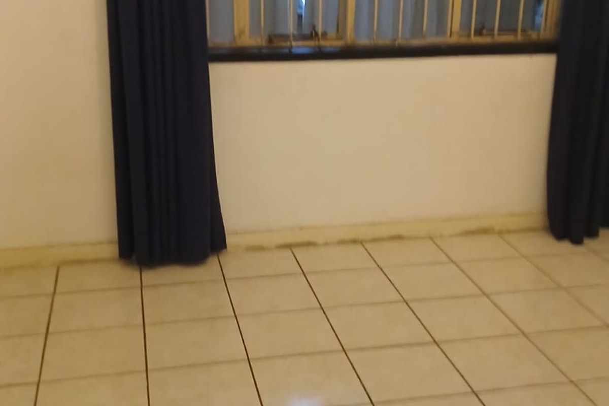 An empty bedroom featuring tiled flooring and security bars on the window, requiring minor cosmetic updates to improve its overall appeal.