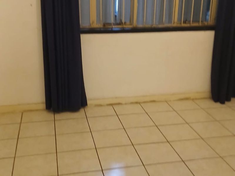 An empty bedroom featuring tiled flooring and security bars on the window, requiring minor cosmetic updates to improve its overall appeal.