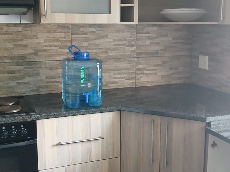Kitchen area featuring light wood-look laminate cabinetry, granite countertops, built-in oven, hob, and extractor fan with a decorative tiled backsplash.