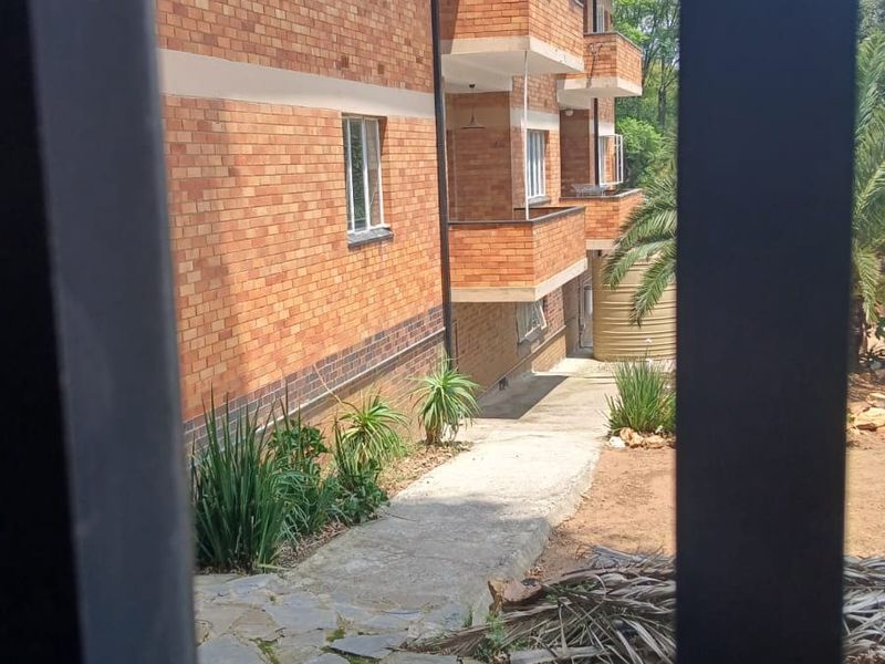 Rear view of a multi-story apartment building featuring face brick construction, private balconies, and a stone-paved garden pathway.