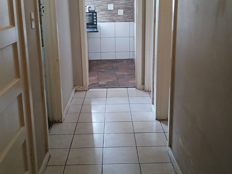 A tiled hallway providing access to multiple rooms, featuring neutral walls and a central ceiling light fixture.