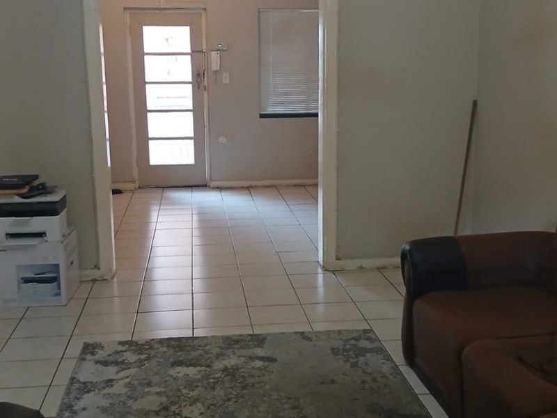 A living area featuring tiled flooring and a central chandelier, leading through to an entrance hall with an external door.