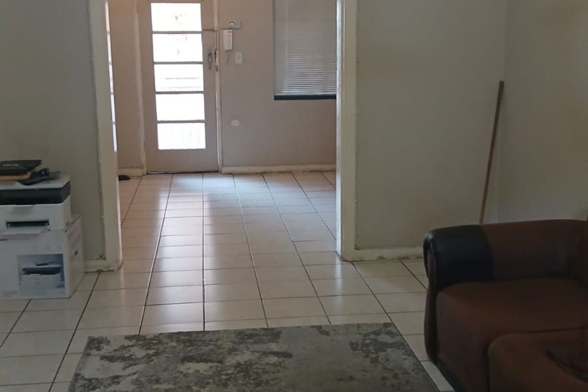 A living area featuring tiled flooring and a central chandelier, leading through to an entrance hall with an external door.