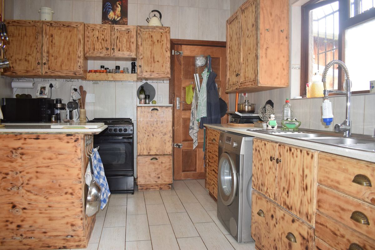 A functional kitchen featuring wooden cabinetry, tiled flooring, a freestanding oven, and a stainless steel sink with a modern gooseneck faucet.