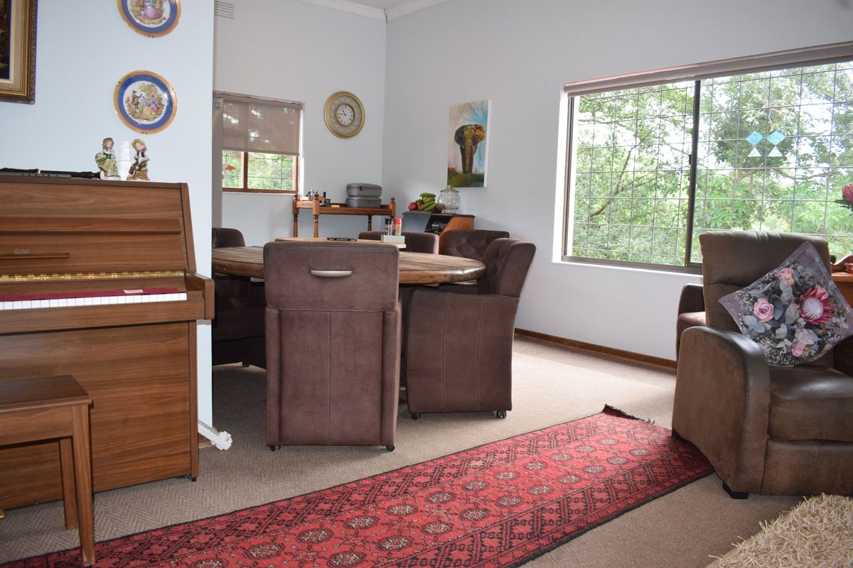 A living and dining area featuring carpeted flooring, large windows with security bars, and decorative cornice detailing.
