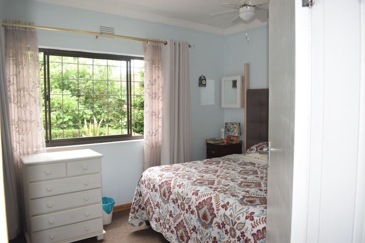 A bedroom featuring a ceiling fan, decorative cornice, and a window with security bars overlooking the garden.