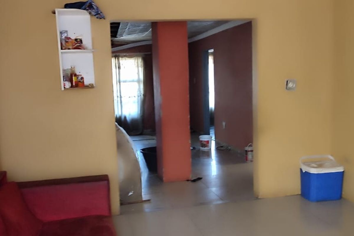 A living area featuring tiled flooring and a central structural pillar, leading into an adjacent room with visible ceiling work required.