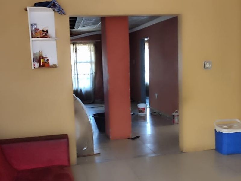 A living area featuring tiled flooring and a central structural pillar, leading into an adjacent room with visible ceiling work required.