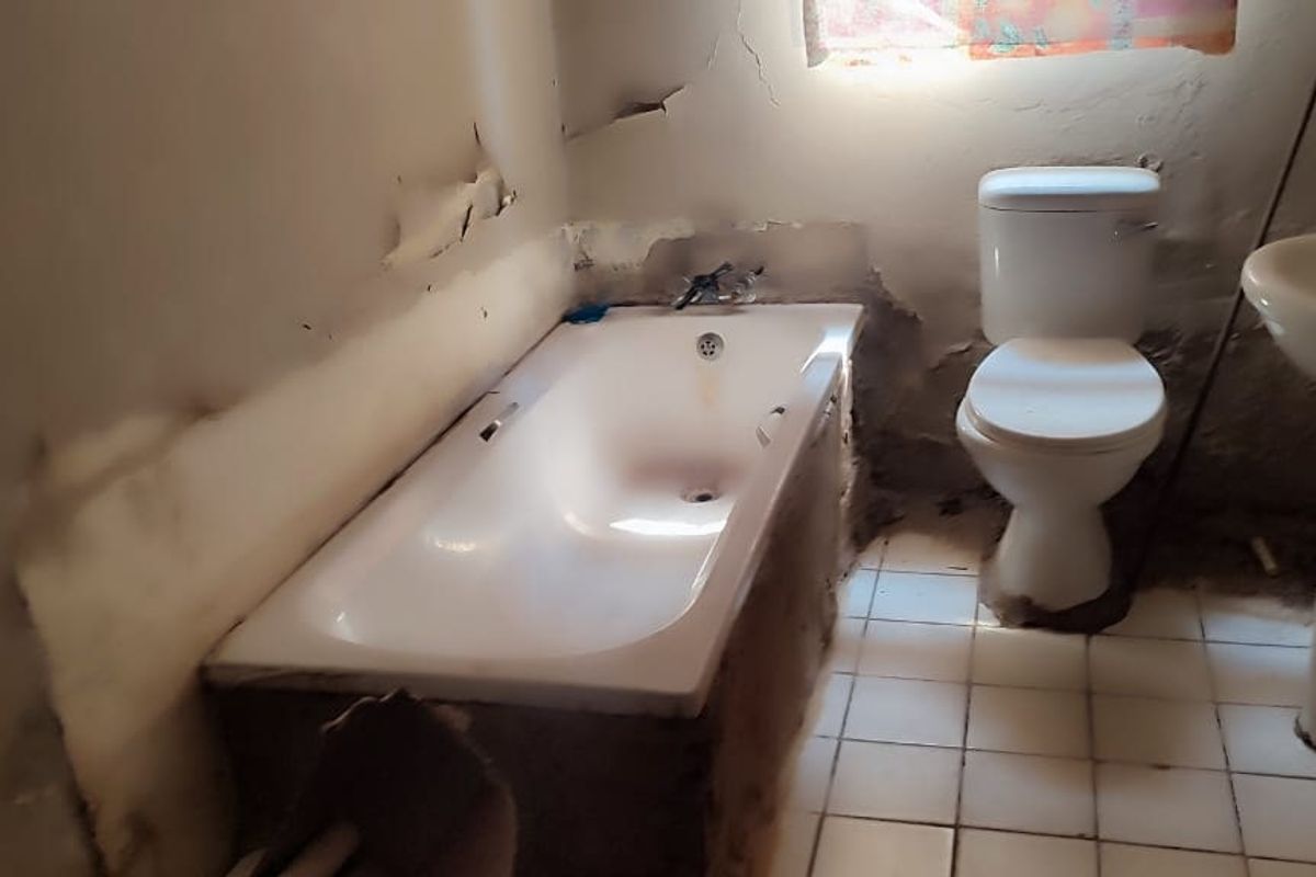 A bathroom in need of significant renovation, featuring a bathtub, toilet, and pedestal basin with visible wall damage and peeling paint.