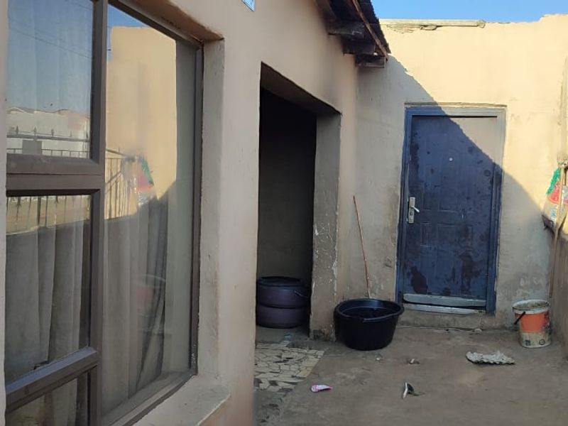 Rear exterior view of the property showing plastered walls, a metal security gate, and access to the building entrance.